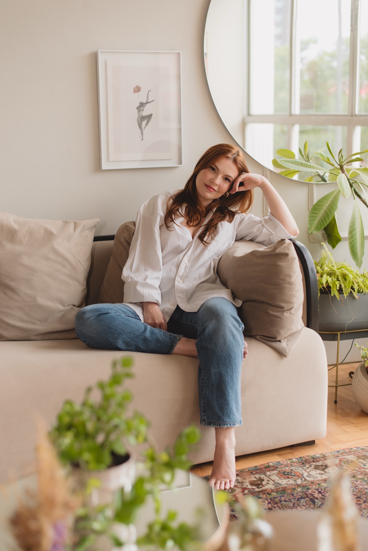 Lorena sentada no sofá do apartamento, plantas em primeiro plano