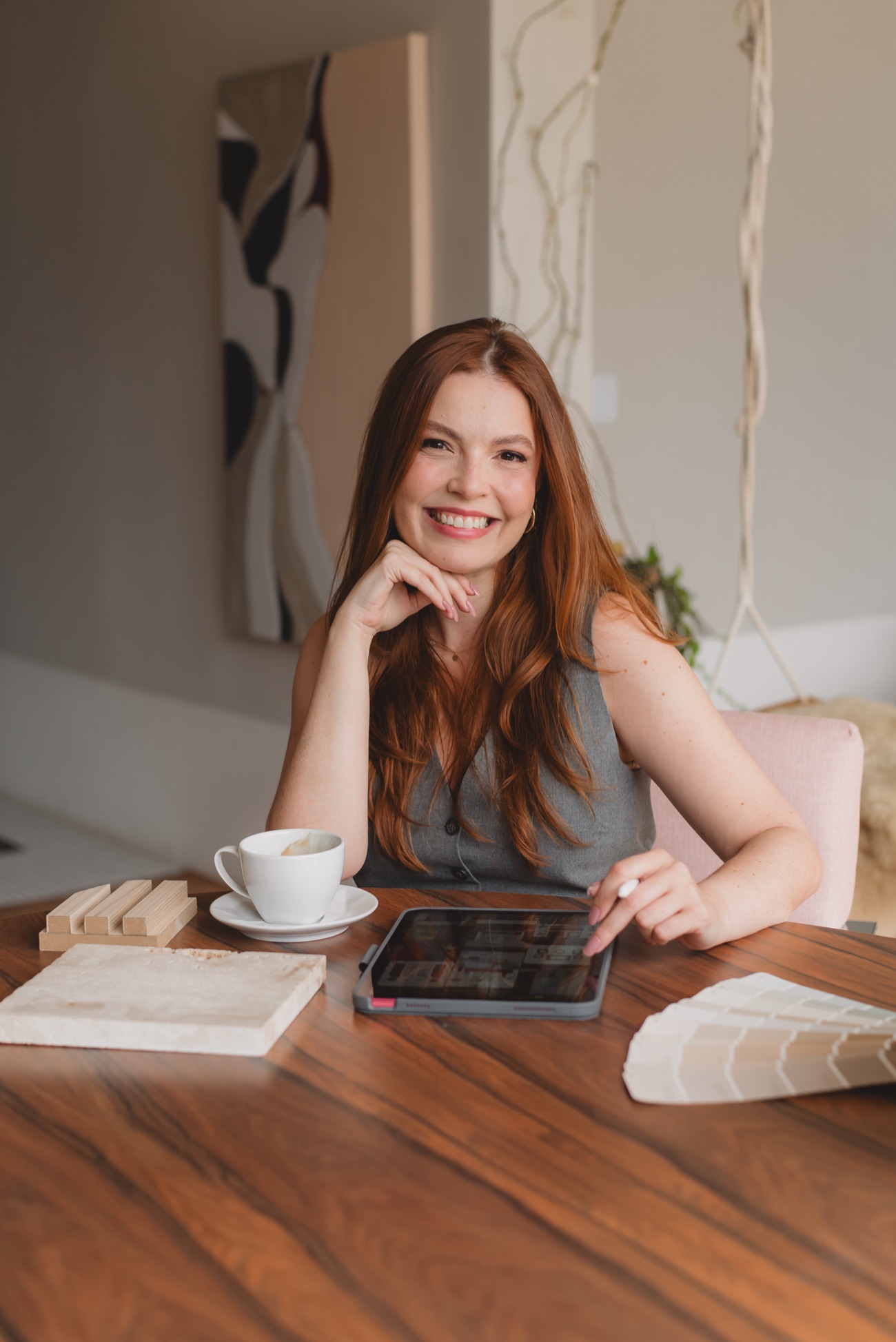 Lorena trabalhando à mesa com tablet, café e amostras de material